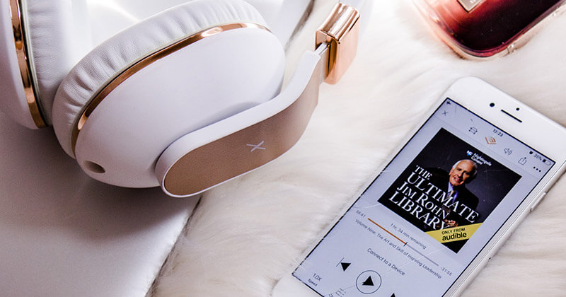 Comment déterminer la taille du fichier audio d'un livre audio Une paire d'écouteurs à côté d'un livre audio de The Ultimate Jim Rohn Library sur un iPhone.